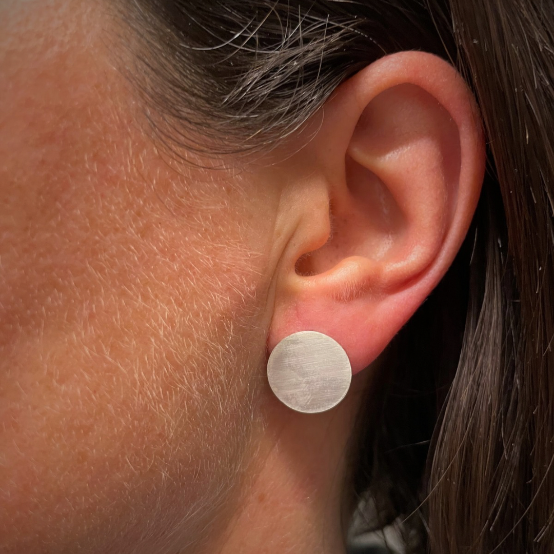 Close up of a woman’s ear who is wearing a circular sterling silver earring that is a full circle with a diameter of 1,5 cm.