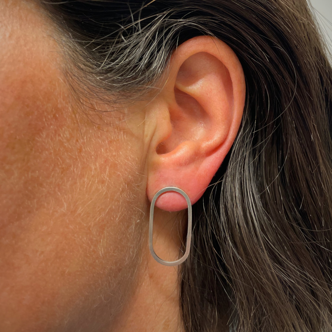 Close up of a woman’s ear who is wearing a sterling silver earring with an elliptical shape that is 2,7 cm long.